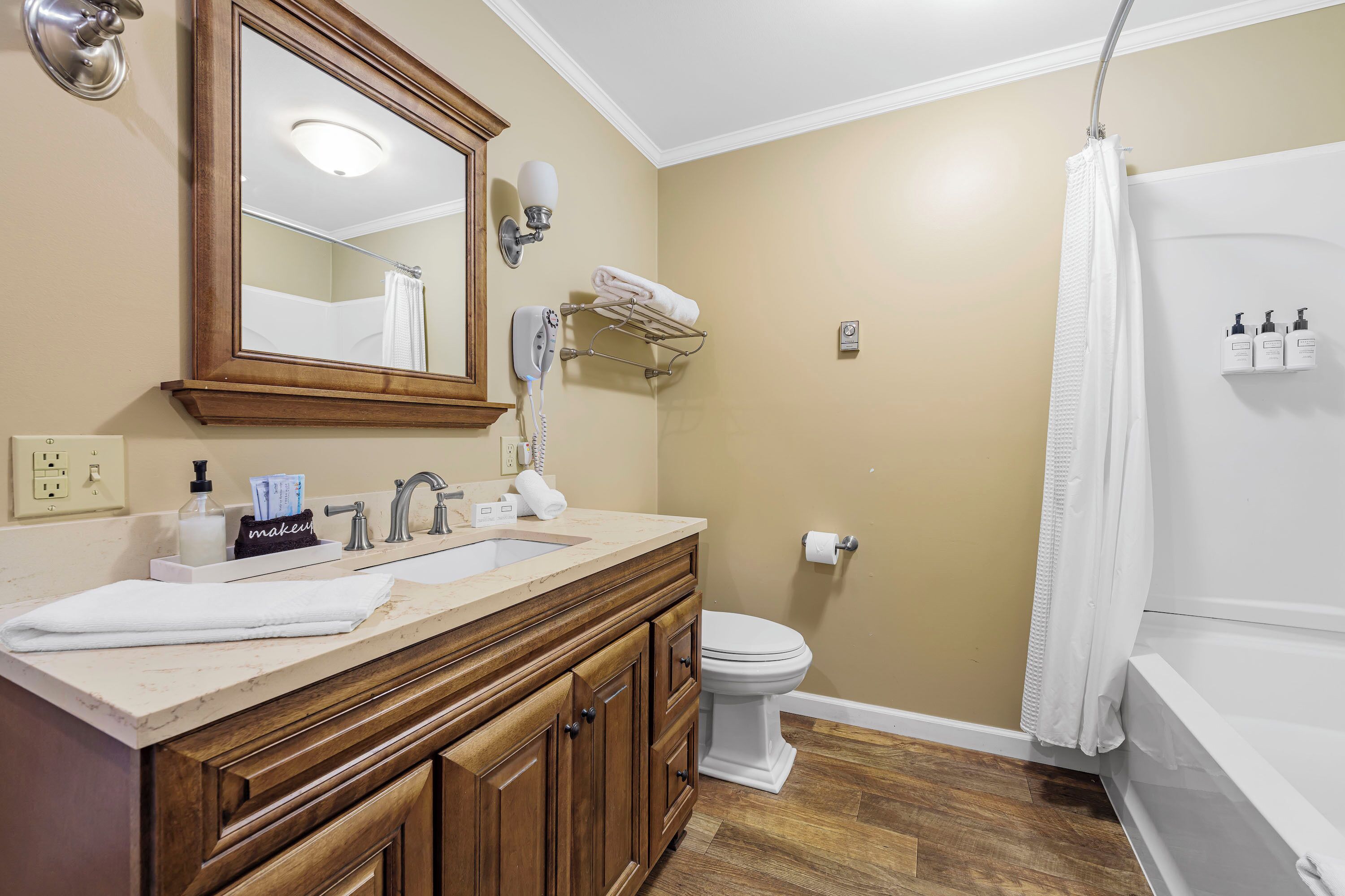 A bathroom with a wooden vanity, a mirror, a toilet, and a shower area.