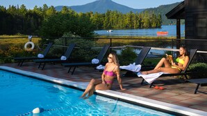 Un espace aménagé au bord de la piscine, avec des chaises longues, une piscine et une vue sur un lac, avec une montagne en arrière-plan.