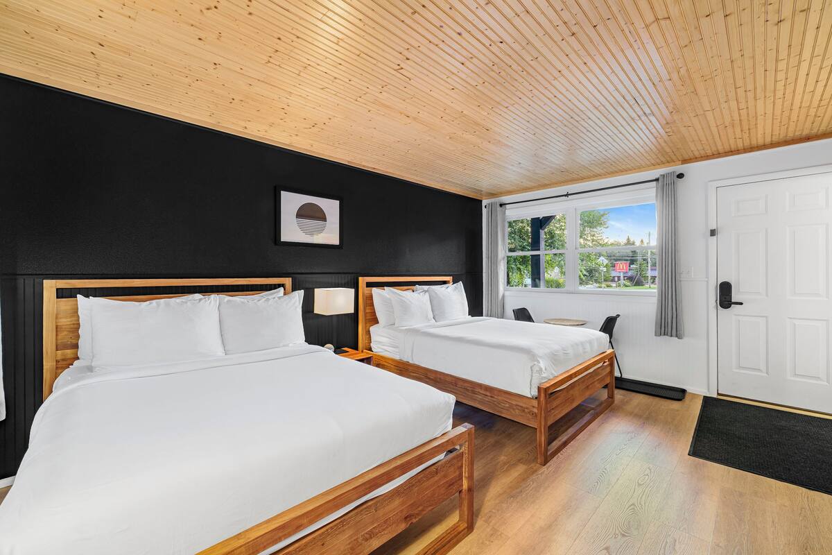 Een kamer met twee houten bedden, een zwarte wand, een houten plafond en een raam met uitzicht op groen.