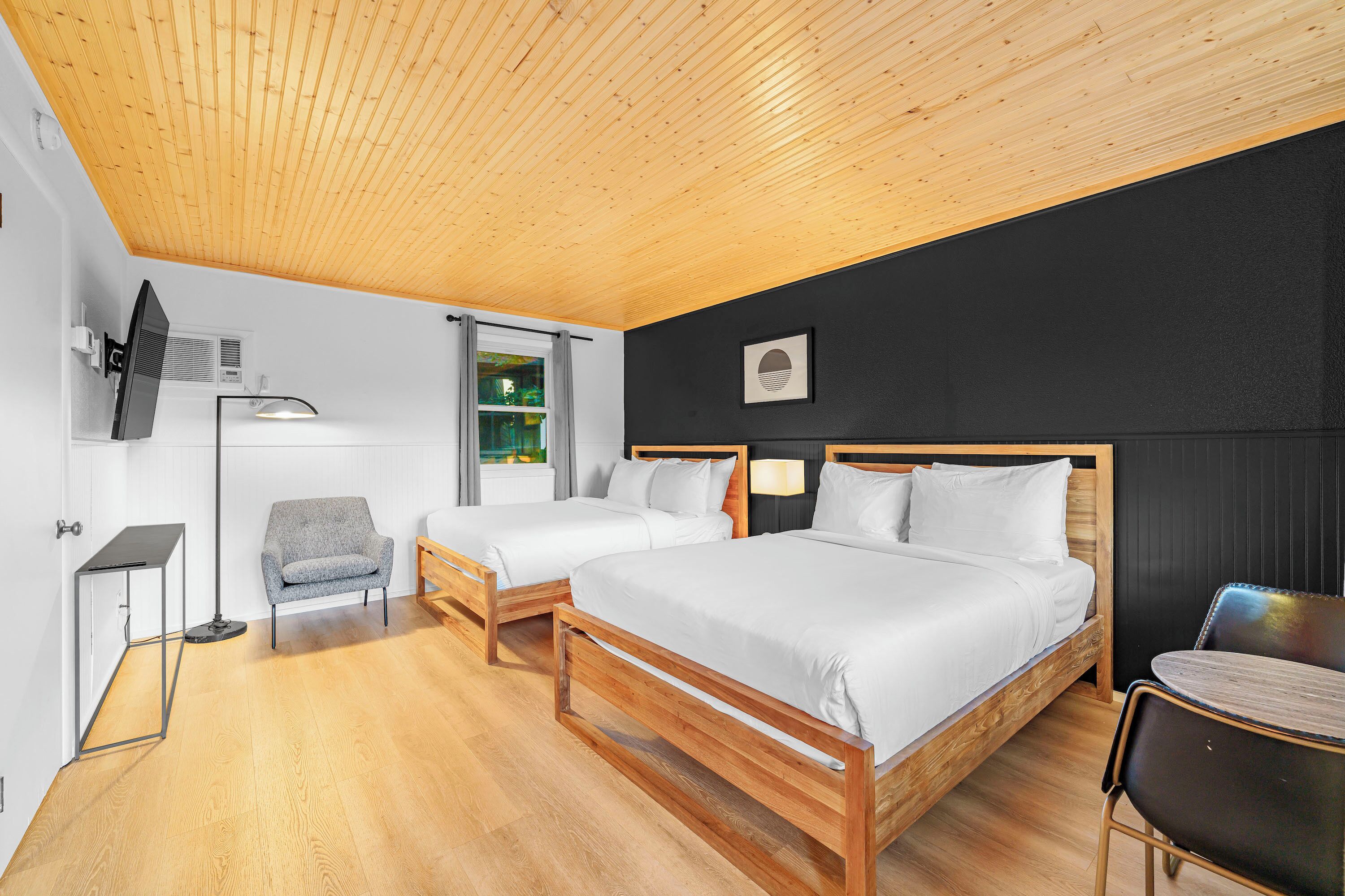 A modern hotel room with two single beds, a desk, a chair, and a TV mounted on the wall.