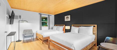 A modern hotel room with two single beds, a desk, a chair, and a TV mounted on the wall.