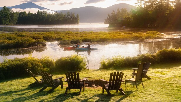Une vue sur le lac, avec des chaises et un kayak, le tout entouré de verdure et de montagnes.