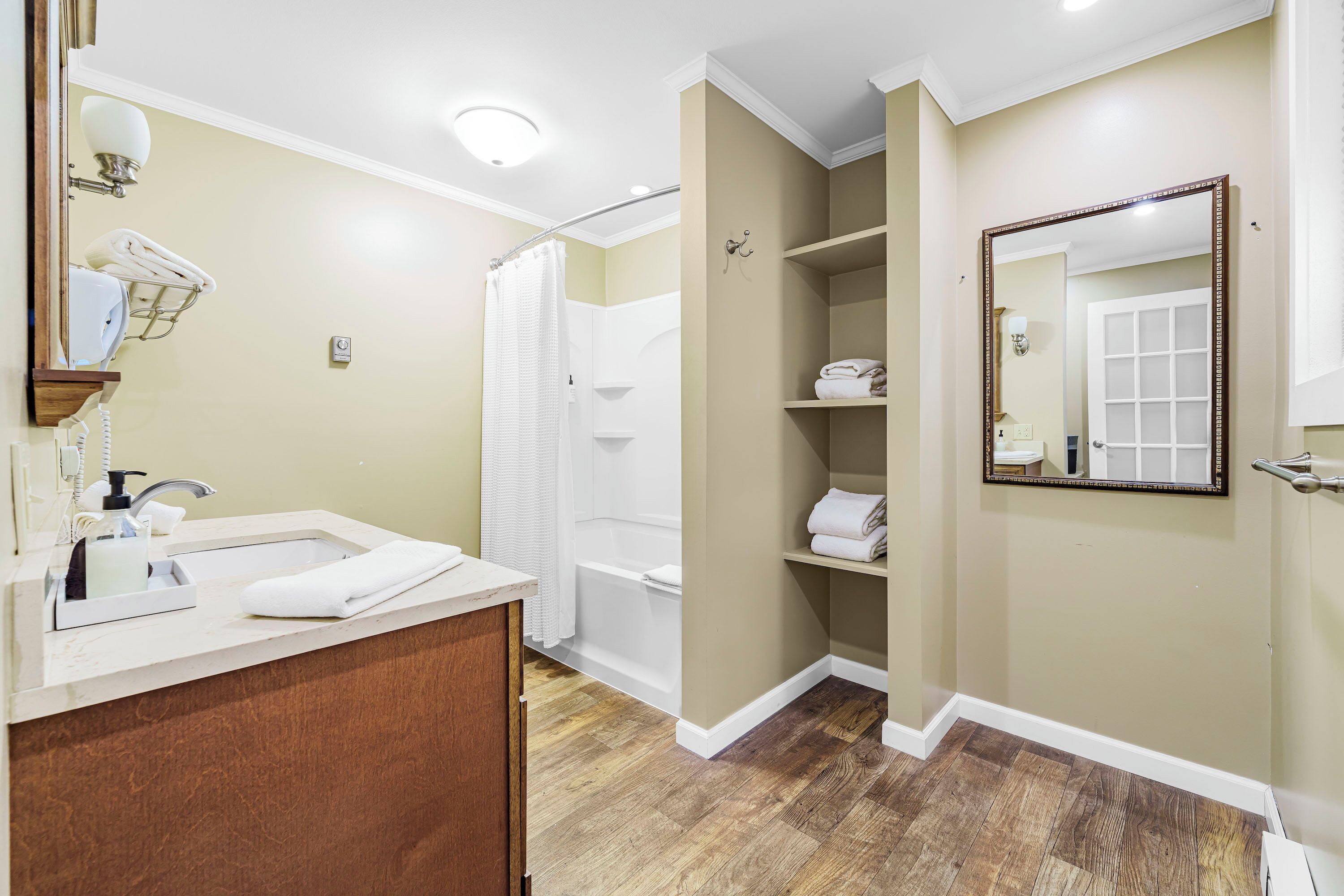 A bathroom with a wooden vanity, a bathtub, a shower, and a mirror with a door.