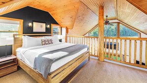 Une chambre à coucher en bois, avec un grand lit, une table de chevet, un ventilateur de plafond et une vue sur l’extérieur.