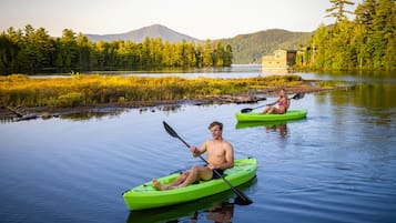 Kayaks await on the calm lake, surrounded by lush greenery and majestic mountains.