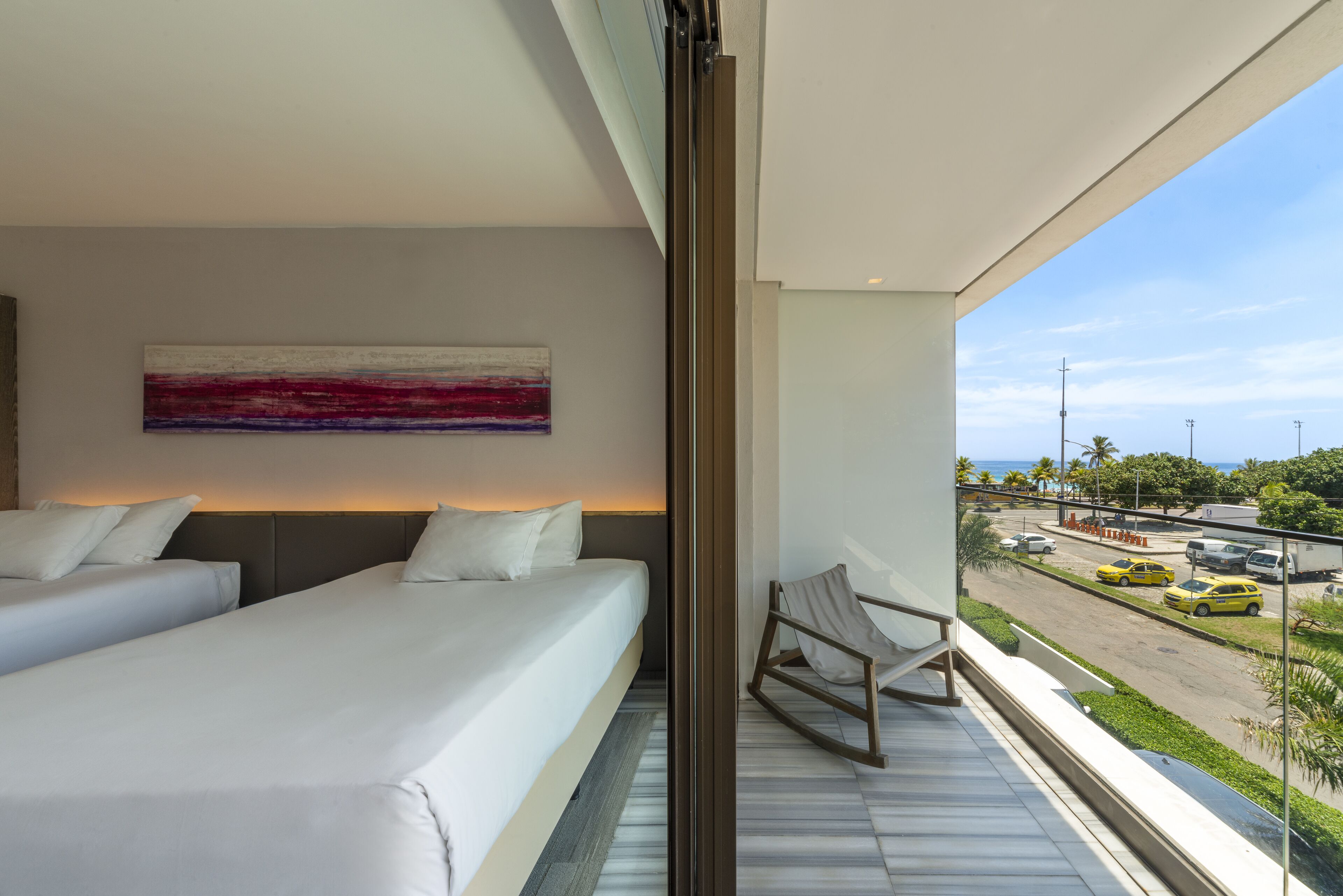 Habitación de hotel moderna con dos camas, vistas a la calle y un balcón con una silla.
