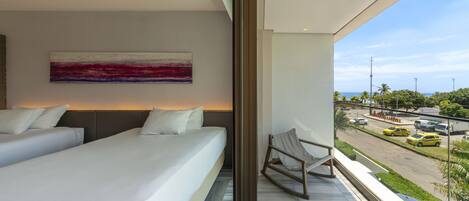 Habitación de hotel moderna con dos camas, vistas a la calle y un balcón con una silla.