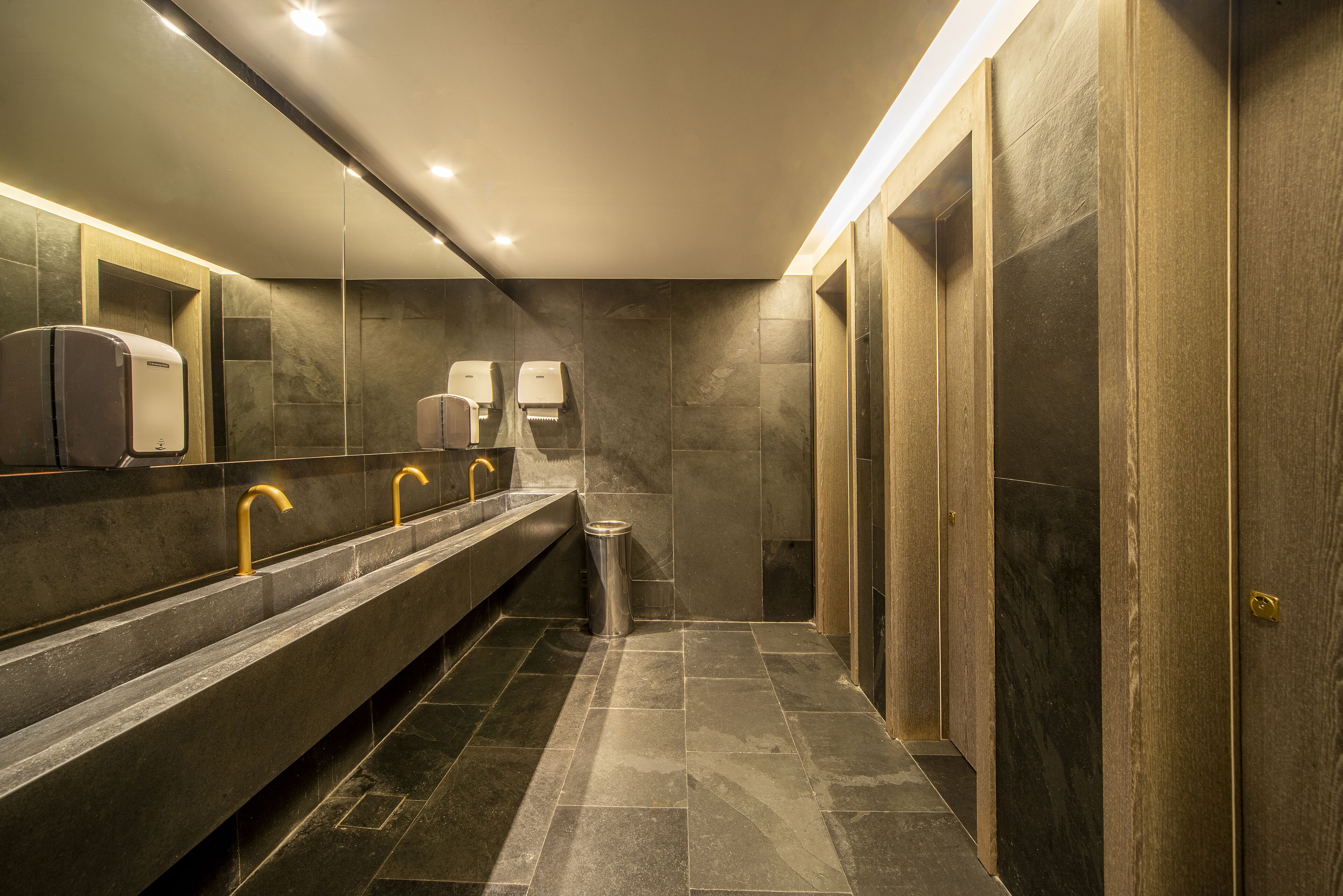 A modern restroom with a long bench, multiple sinks, and hand dryers.