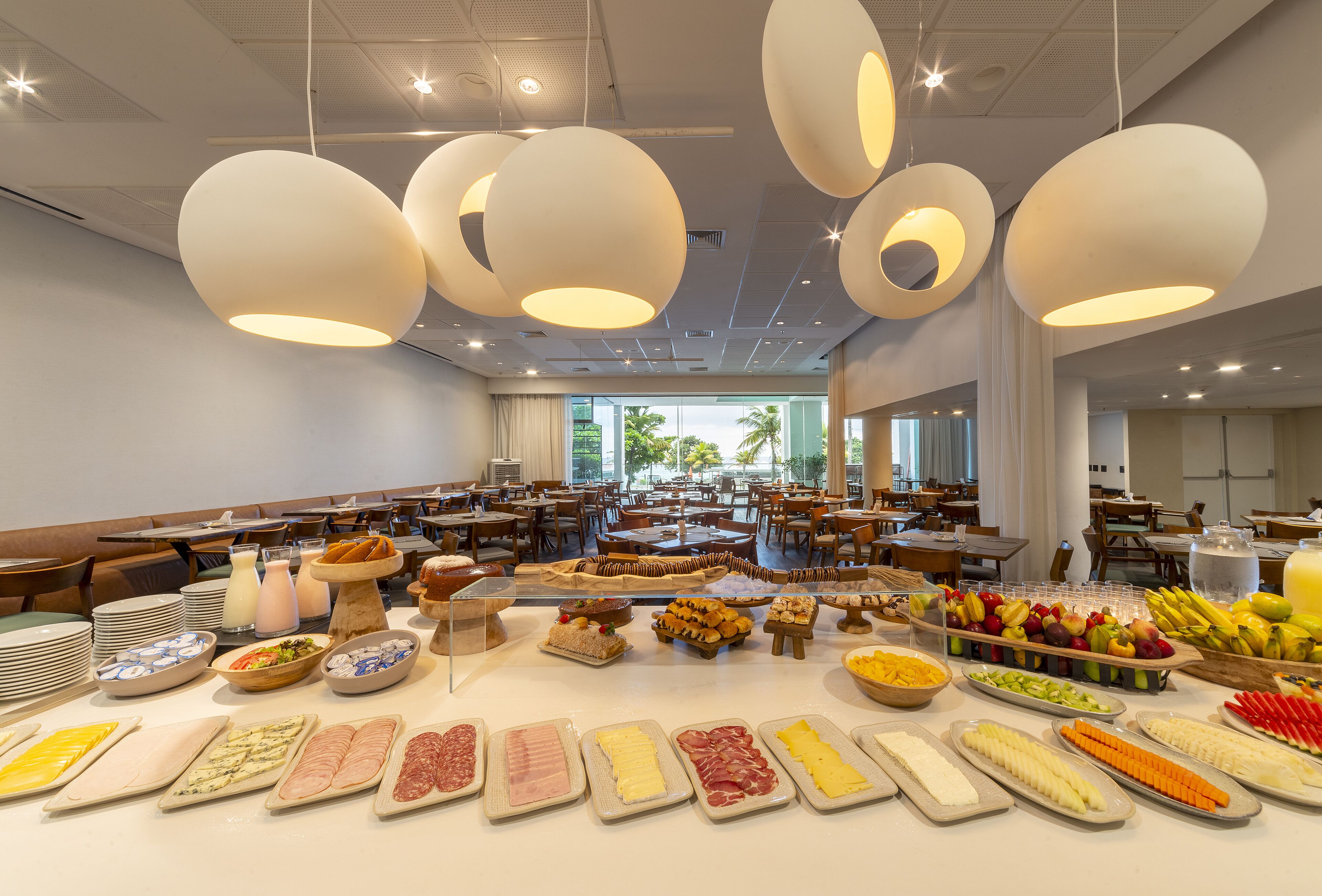 Ein reichhaltiges Buffet mit verschiedenen Speisen und einem modernen Interieur, das von hängenden, kugelförmigen Leuchten geprägt ist.