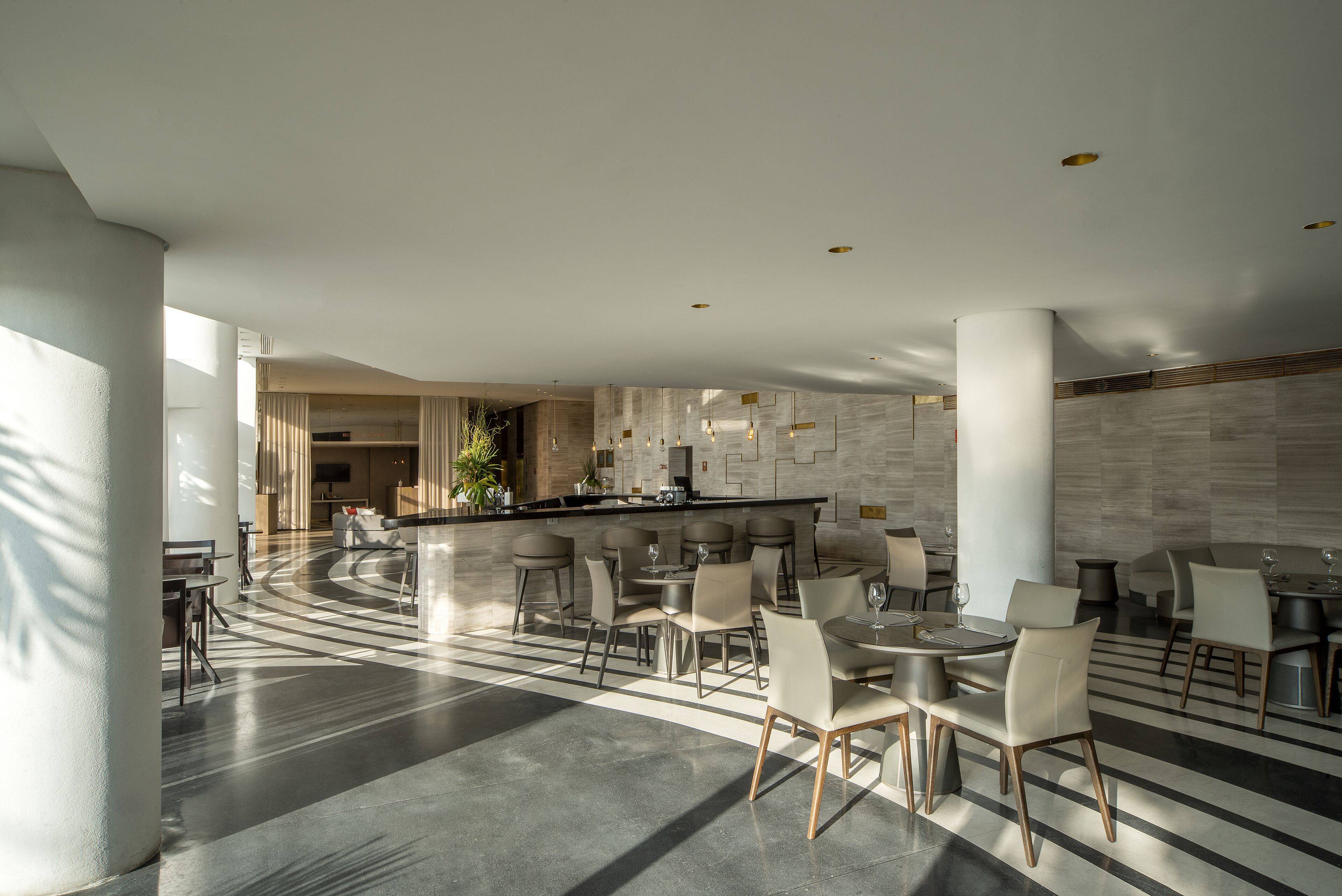 A modern hotel lobby with a central bar, seating areas, and a large open space with a patterned floor.