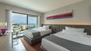 Quarto de hotel com duas camas, uma escrivaninha e vista para a cidade e o mar.