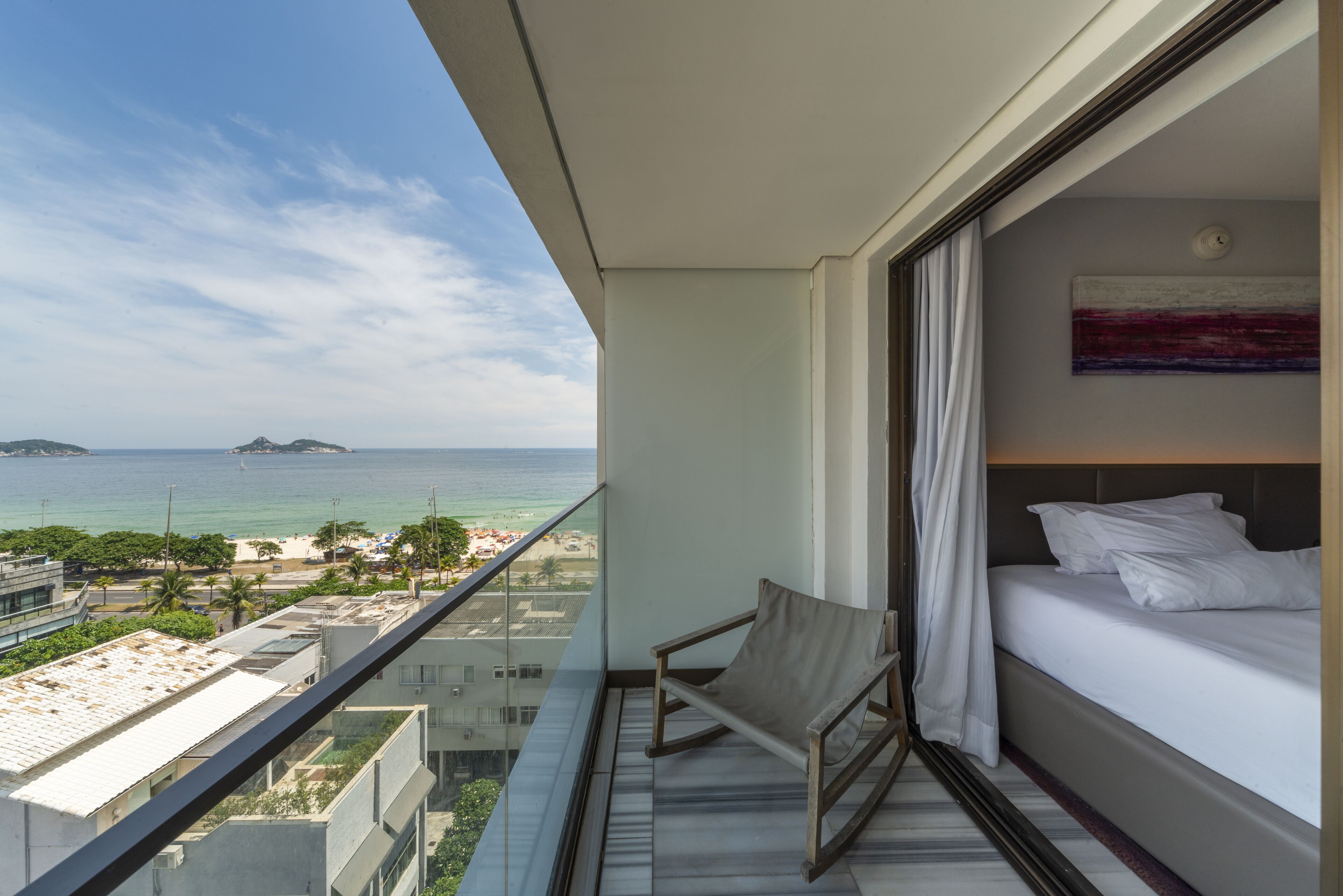 A balcony with a bed and a chair, overlooking a beach and ocean.