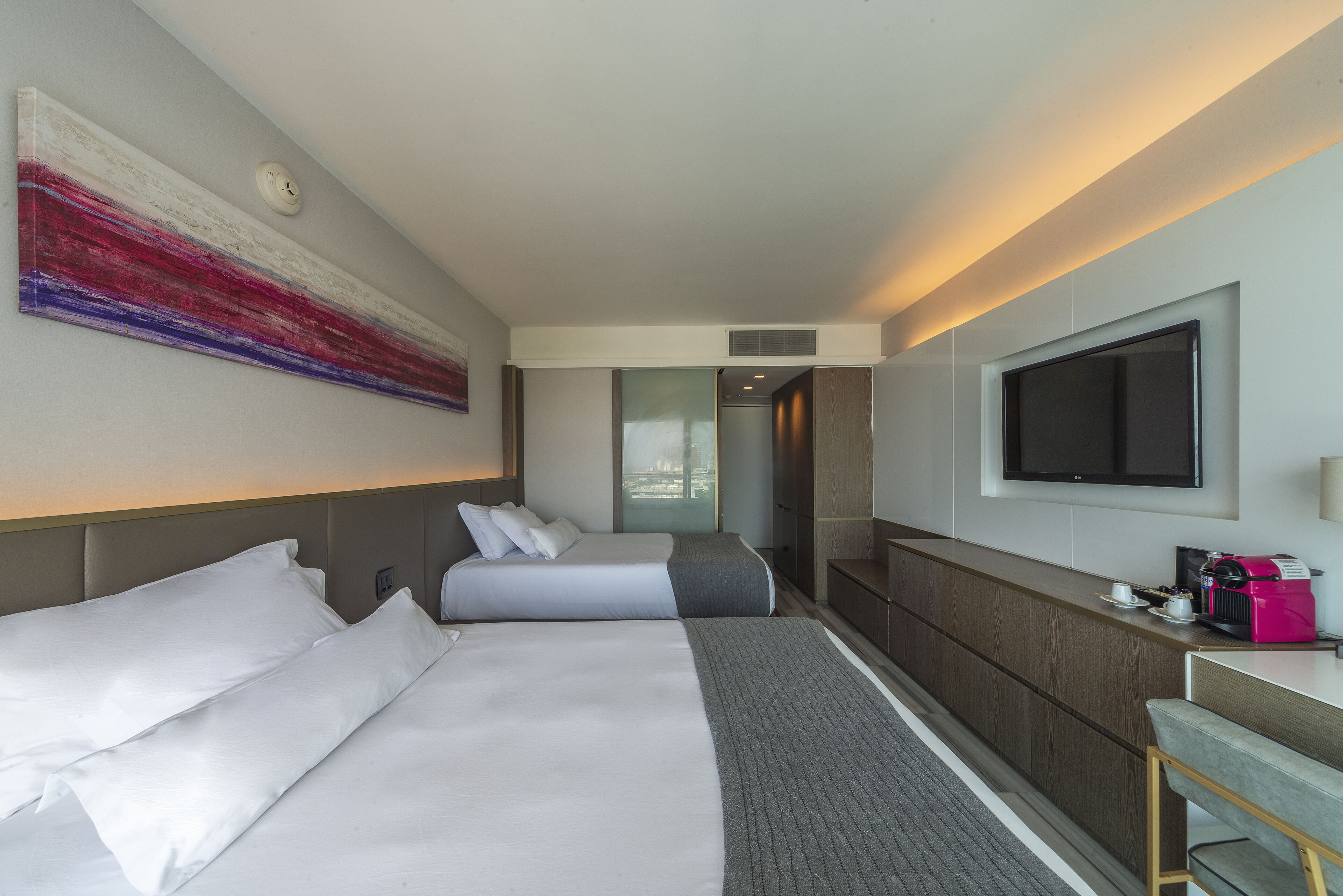 Habitación de hotel con dos camas, televisión, escritorio y un cuadro abstracto grande en la pared.