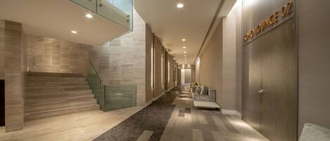 Een moderne hotellobby met een glazen trap, een bank en een bord met de tekst 'SOHO LOUNGE 02'.