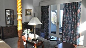 Un dormitorio con cama, tocador, lámpara, silla, mesa y vista al exterior a través de una puerta.