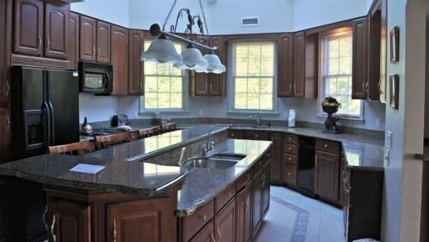 Una cocina amplia con armarios de madera oscura, una isla grande con lavamanos e iluminación colgante.