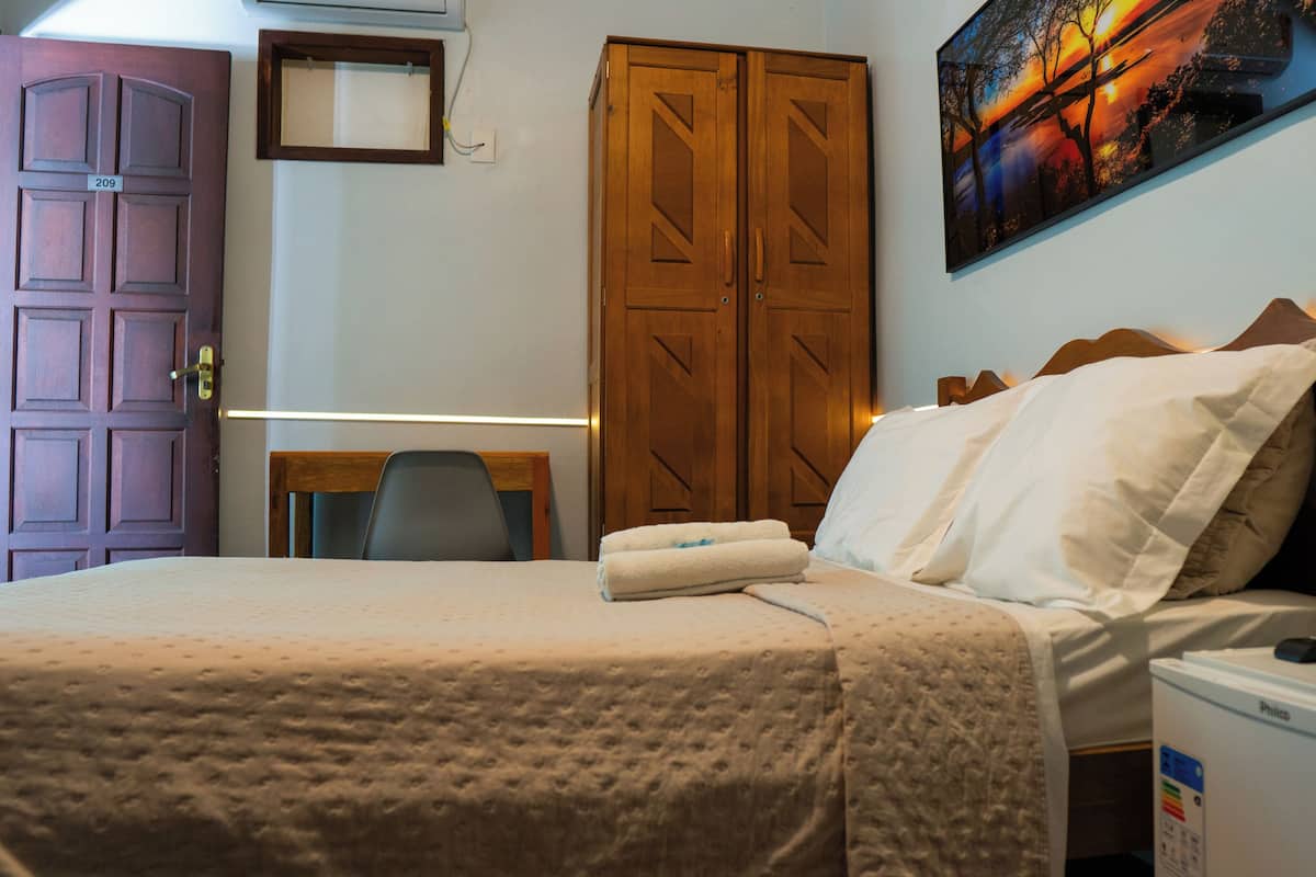 Ein Hotelzimmer mit Bett, Schreibtisch, Stuhl, Kleiderschrank und einem Bild an der Wand.