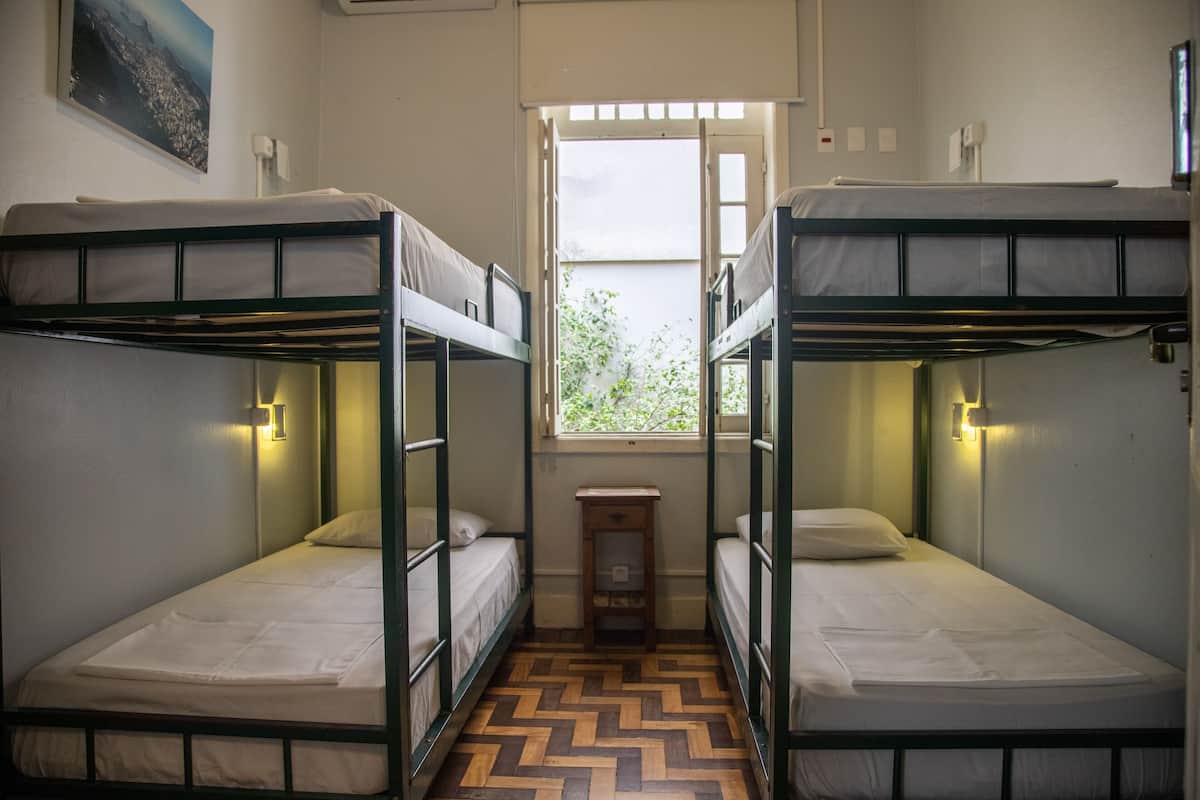 Ein Schlafsaalzimmer mit Etagenbetten, einem kleinen Fenster und einem Holzboden.