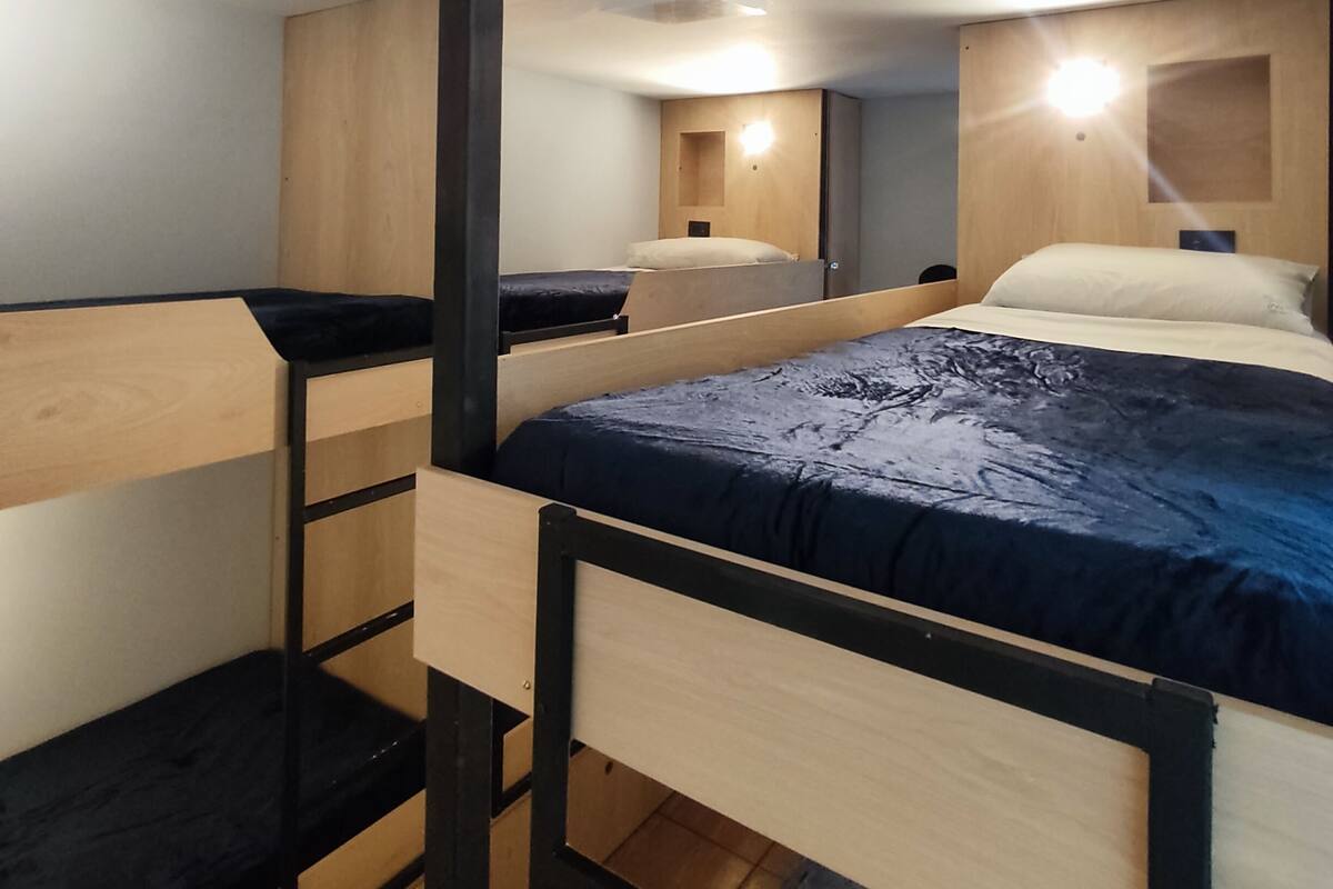 Ein Schlafsaal mit Etagenbetten, Holzbalken, einem Schreibtisch und einem Spiegel.