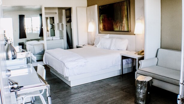 A modern hotel room with a large bed, a desk, a chair, a small table, and a sofa. - Devonshire Inn (Rosamond)