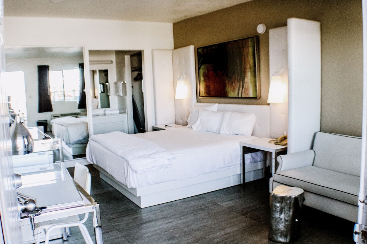 Una habitación de hotel moderna con una cama grande, un escritorio, una silla, una mesita y un sofá.