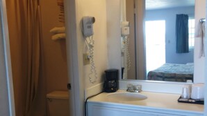 A bathroom with a toilet, a sink, a mirror, a hairdryer, and a shower curtain. - Devonshire Inn (Rosamond)
