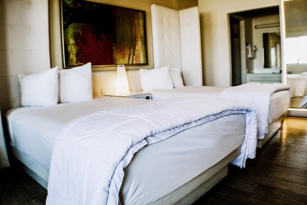 Habitación de hotel con dos camas, un cuadro grande en la pared y un baño visible a través de una puerta abierta.