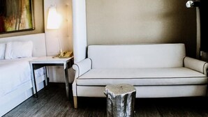 A hotel room with a bed, a sofa, a small table, a lamp, and a wooden stool. - Devonshire Inn (Rosamond)