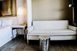 A hotel room with a bed, a sofa, a small table, a lamp, and a wooden stool. - Devonshire Inn (Rosamond)