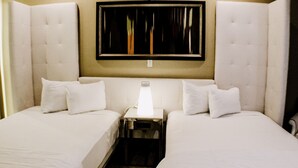 A hotel room with two beds, a nightstand, a wall-mounted clock, and a window with blinds. - Devonshire Inn (Rosamond)