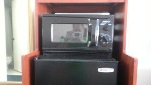 A black refrigerator with a microwave on top, placed in a wooden cabinet. - Devonshire Inn (Rosamond)