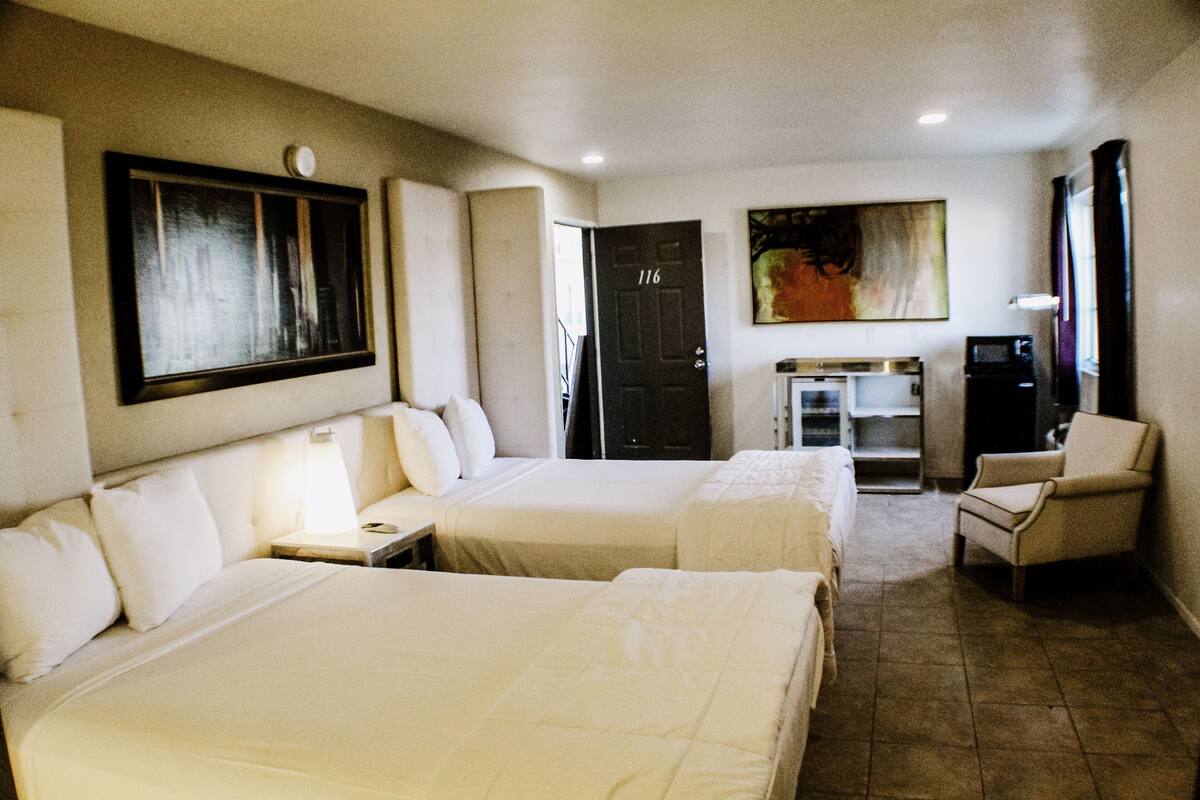 Habitación de hotel con dos camas, un escritorio, una silla, un televisor y una puerta con el número 116.