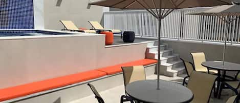Una terraza en la azotea con piscina, zona de estar y mesas al aire libre.