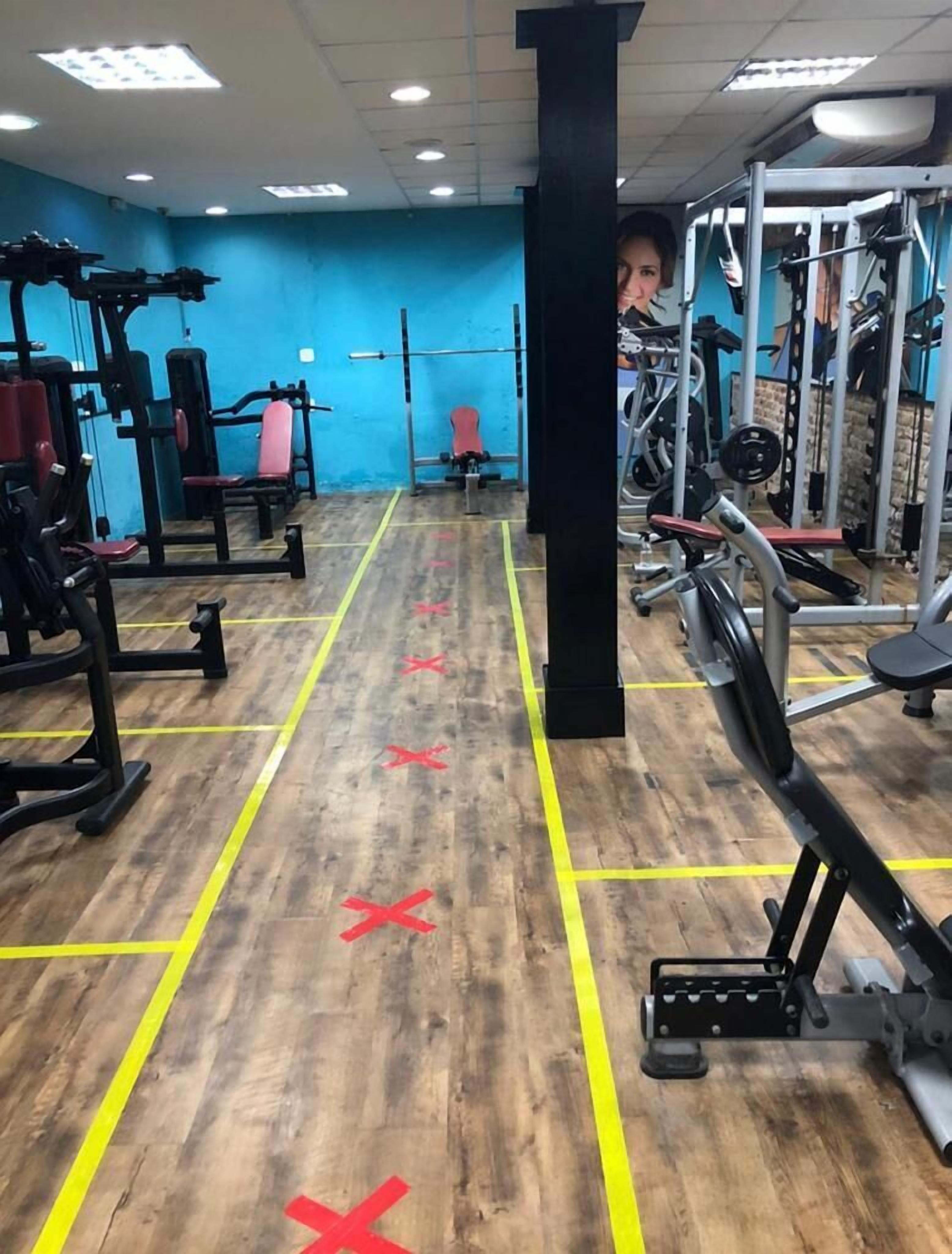 Une salle de sport équipée de divers appareils d’exercice, dotée d’un plancher en bois et de murs bleus.