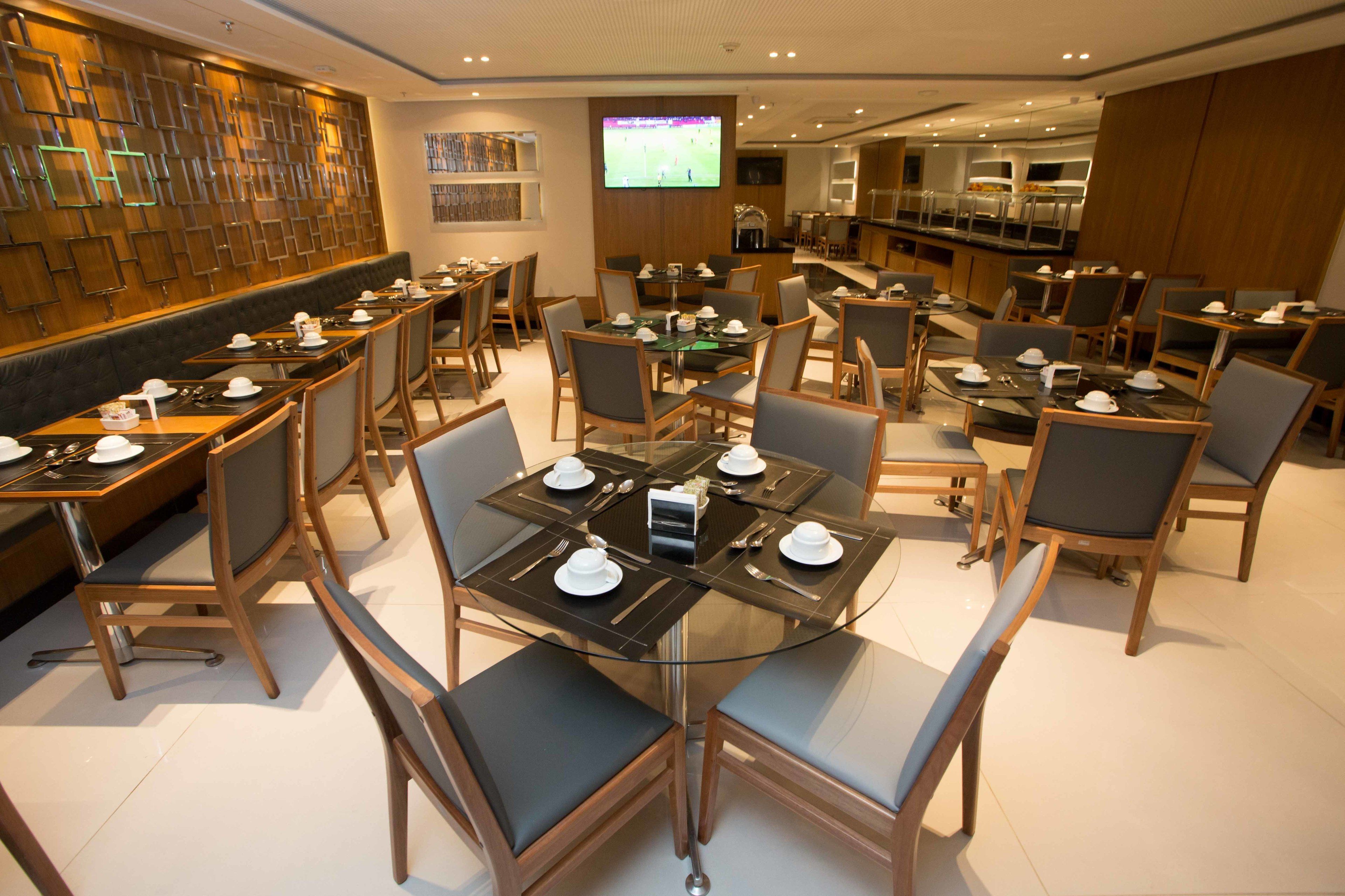 A modern dining area with multiple tables and chairs, a television screen, and a wall with a geometric pattern.
