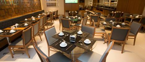 A modern dining area with multiple tables and chairs, a television screen, and a wall with a geometric pattern.