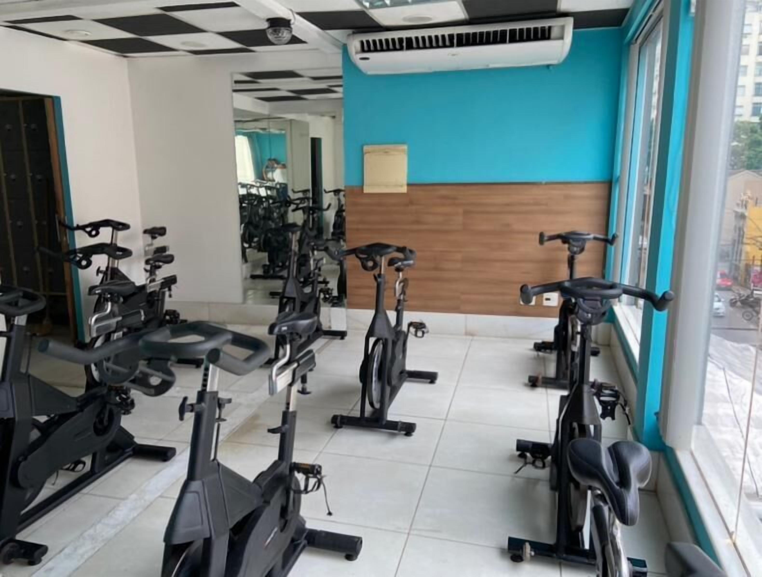 Un gimnasio con bicicletas estáticas dispuestas en filas, una pared azul y una ventana con vista a la calle.