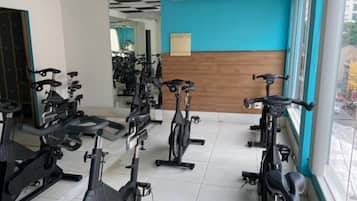 Un gimnasio con bicicletas estáticas dispuestas en filas, una pared azul y una ventana con vista a la calle.