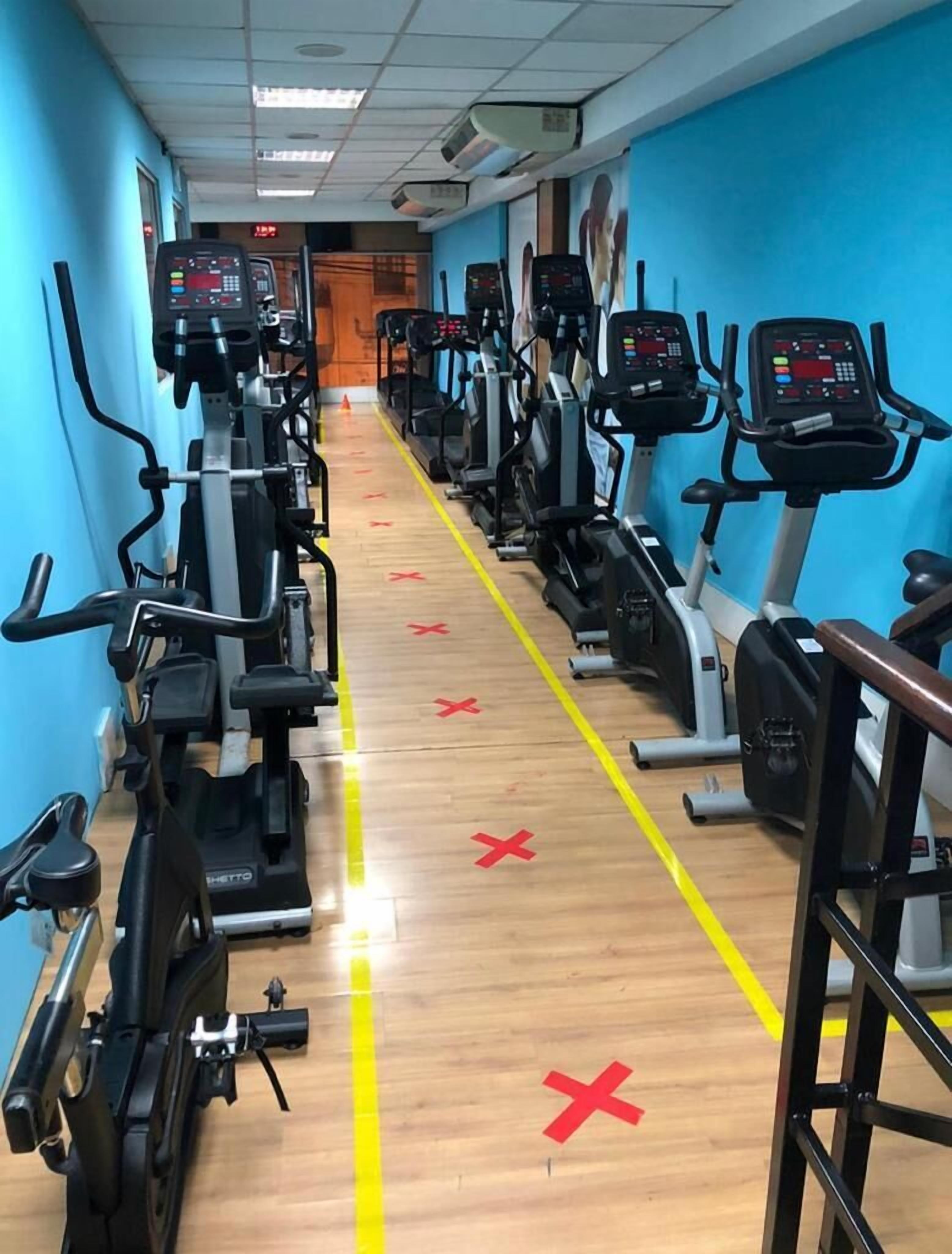 Une salle de sport avec plusieurs rangées de vélos d’appartement et de tapis de course, un plancher en bois et des murs bleus.