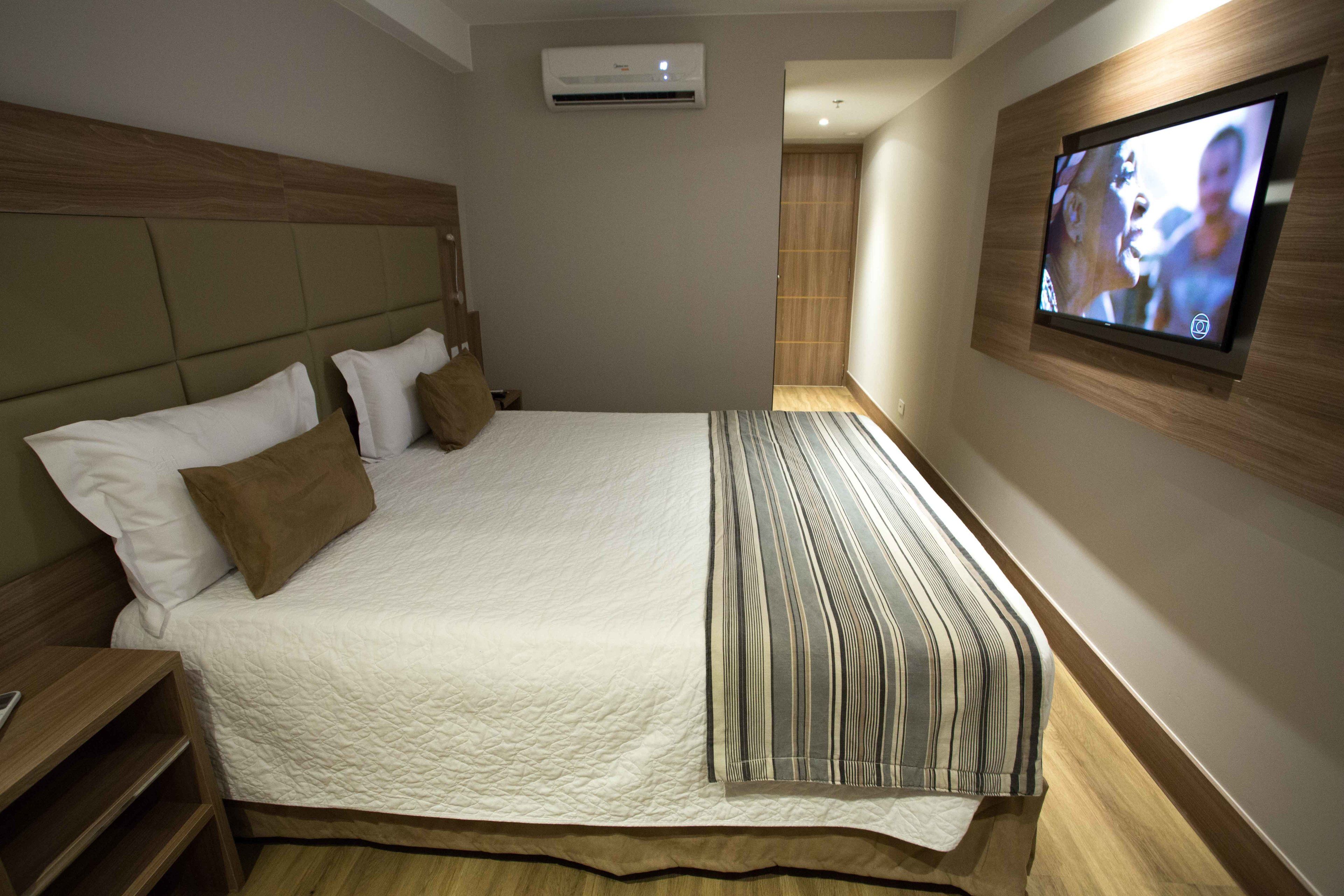 A neatly made bed with a striped blanket, a wooden headboard, and a wall-mounted TV.
