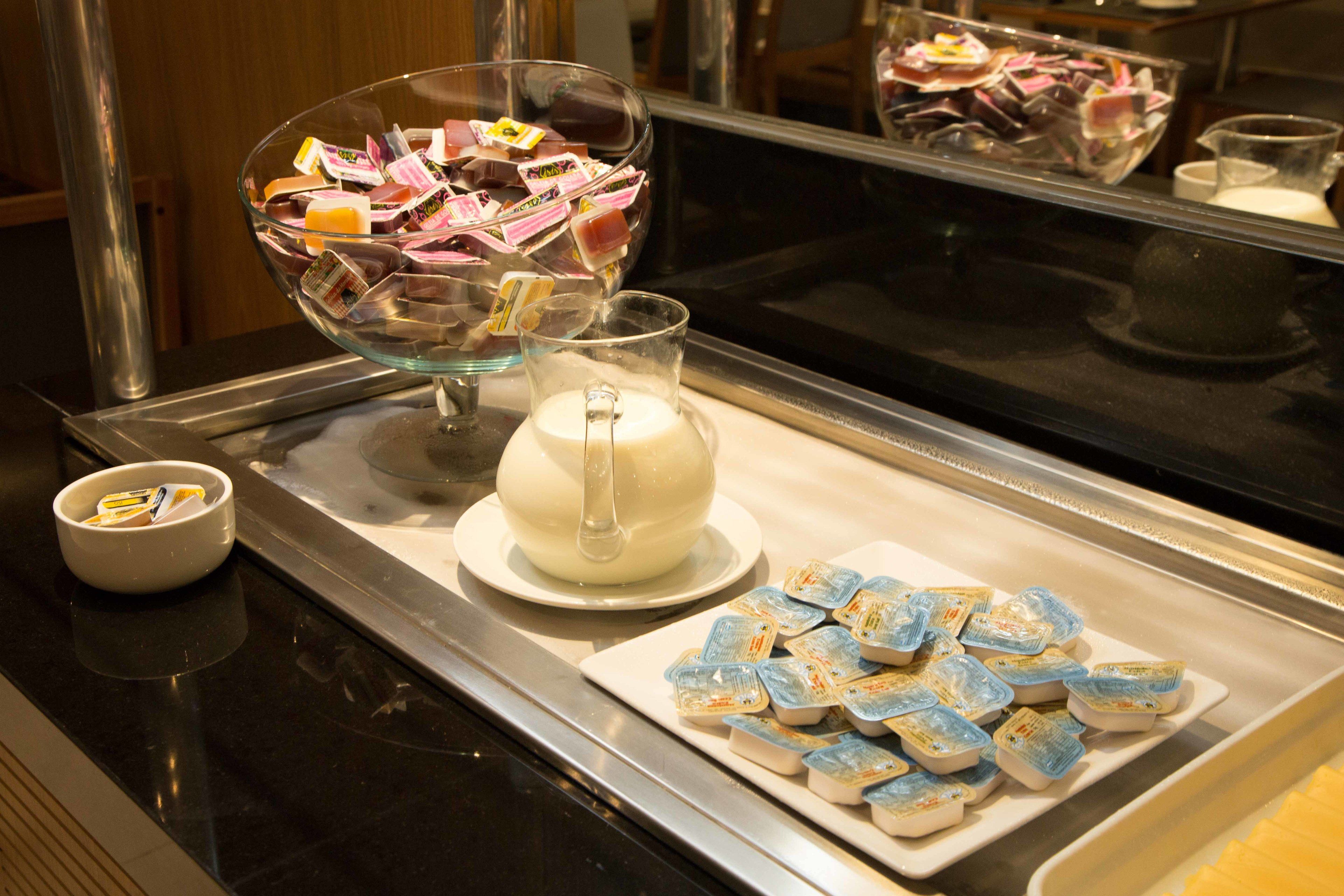A buffet with various food items, including a bowl of assorted snacks, a pitcher of milk, and a plate of yogurt.