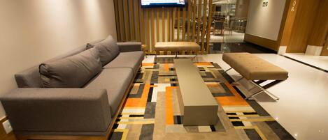 Ein modernes Wohnzimmer mit einer Couch, einem Hocker und einem an der Wand befestigten Fernseher.