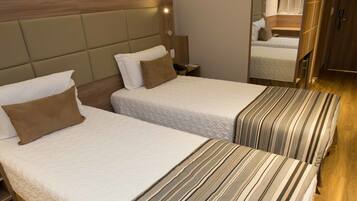 Two single beds with headboards, a wooden floor, an air conditioning unit, and a mirror in the room.