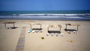 Una playa con tumbonas y estructuras de madera, presumiblemente para dar sombra, a lo largo de un sendero arenoso.