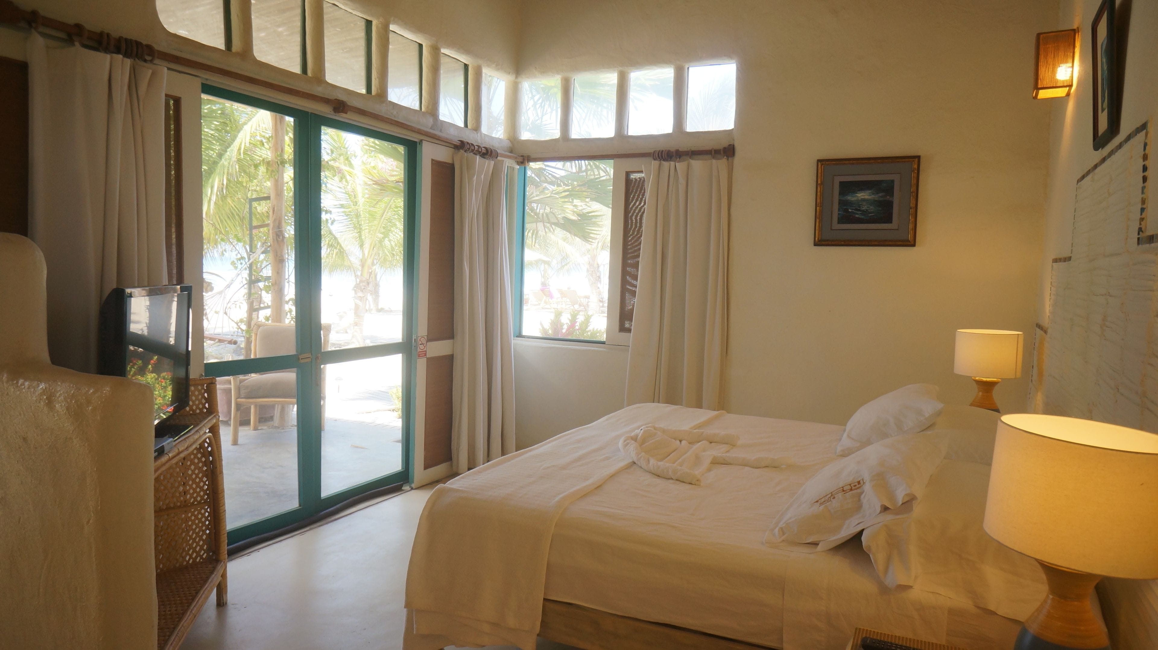 A hotel room with a bed, a TV, a lamp, and a view of the outdoors.