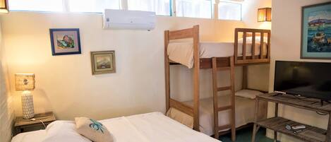 A room with a bunk bed, a desk with a television, and a lamp on a nightstand.