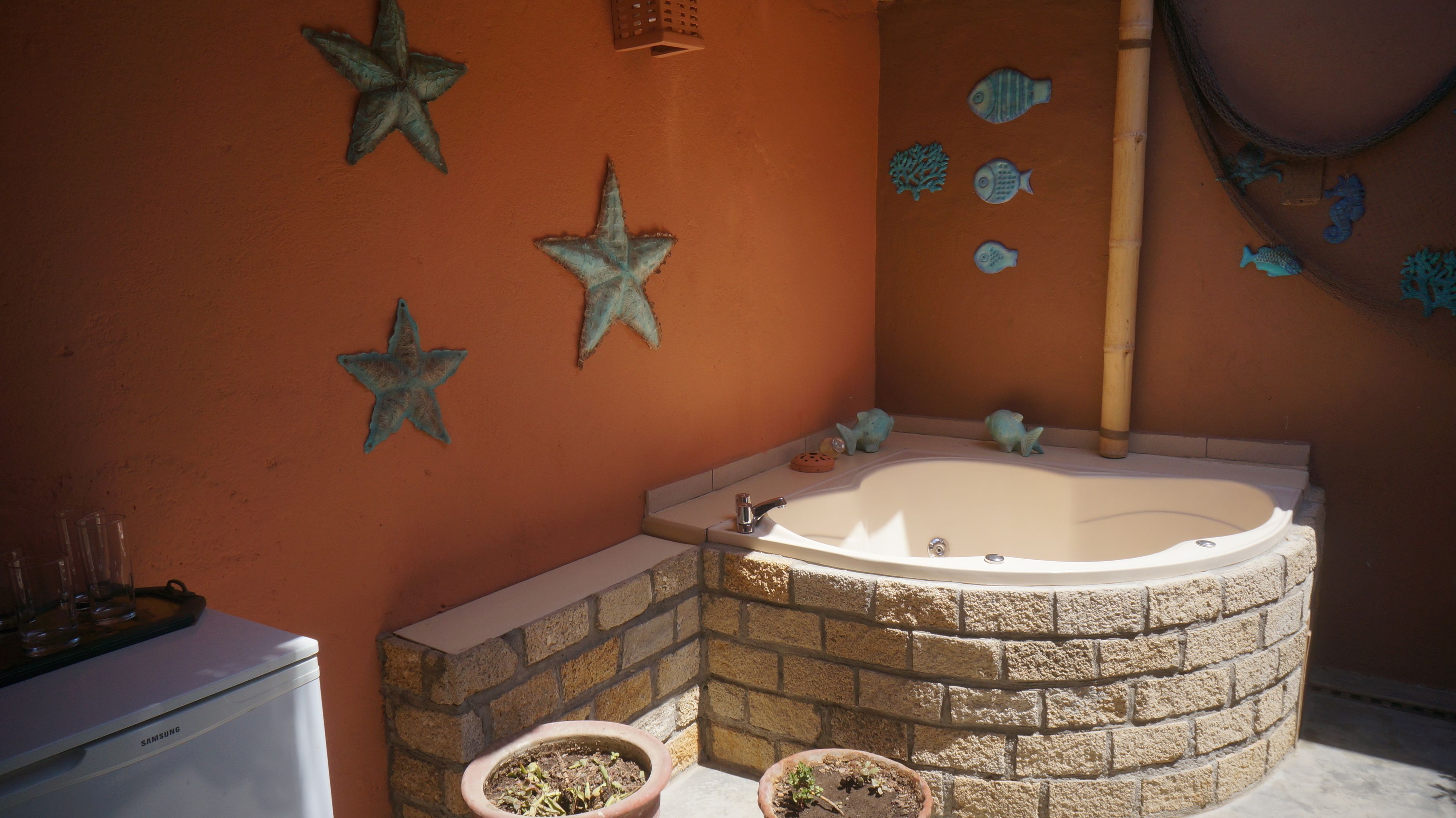 Baño con bañera de piedra, estrellas de mar decorativas y arte mural con peces.