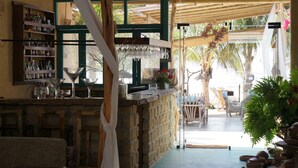 Una zona de bar con mostrador de piedra, estanterías con botellas y vistas al área de mesas al aire libre.