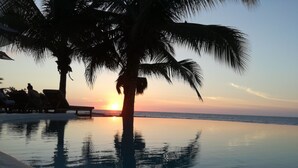 Tranquila vista de la piscina al atardecer, con palmeras y sillas de descanso.