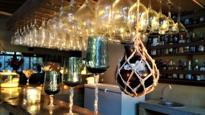 Una zona de bar con varias copas y botellas de vino, estantes llenos de botellas y un lavabo.